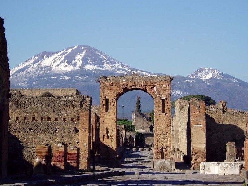 A brick arch at the head of the Forum at Pompeii with snow lying on Mount Vesuvius behind it