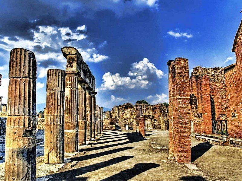 A row of brick and stone columns at Pompeii against a deep blue sky